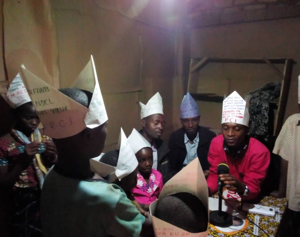 Groupe d'enfants et de jeunes participant à un atelier interactif de Jeunes Solutions, portant des chapeaux en papier et échangeant avec un microphone.