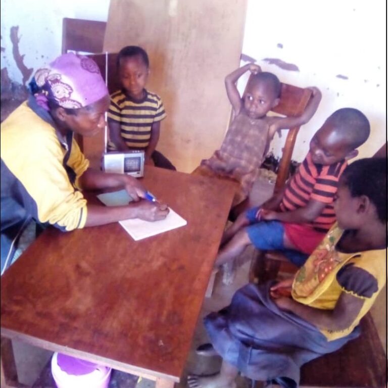 Une mère explique le cours à ses enfants réunis autour d'un poste radio dans le cadre du projet éducatif de Jeunes Solutions.