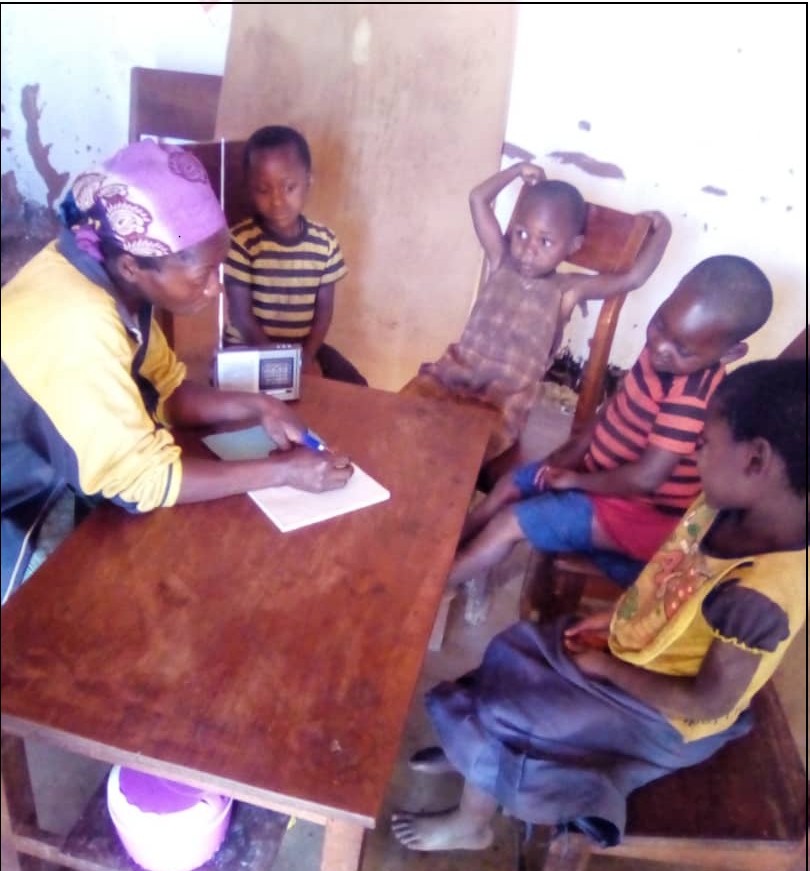 Une mère explique le cours à ses enfants réunis autour d'un poste radio dans le cadre du projet éducatif de Jeunes Solutions.