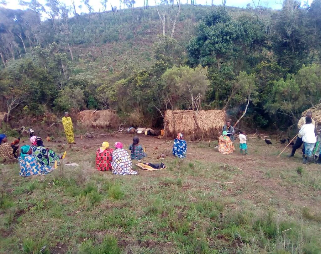 Femmes et filles en tenues traditionnelles colorées réunies dans un village rural sous des paillottes, participant à un programme d'autonomisation de Jeunes Solutions.